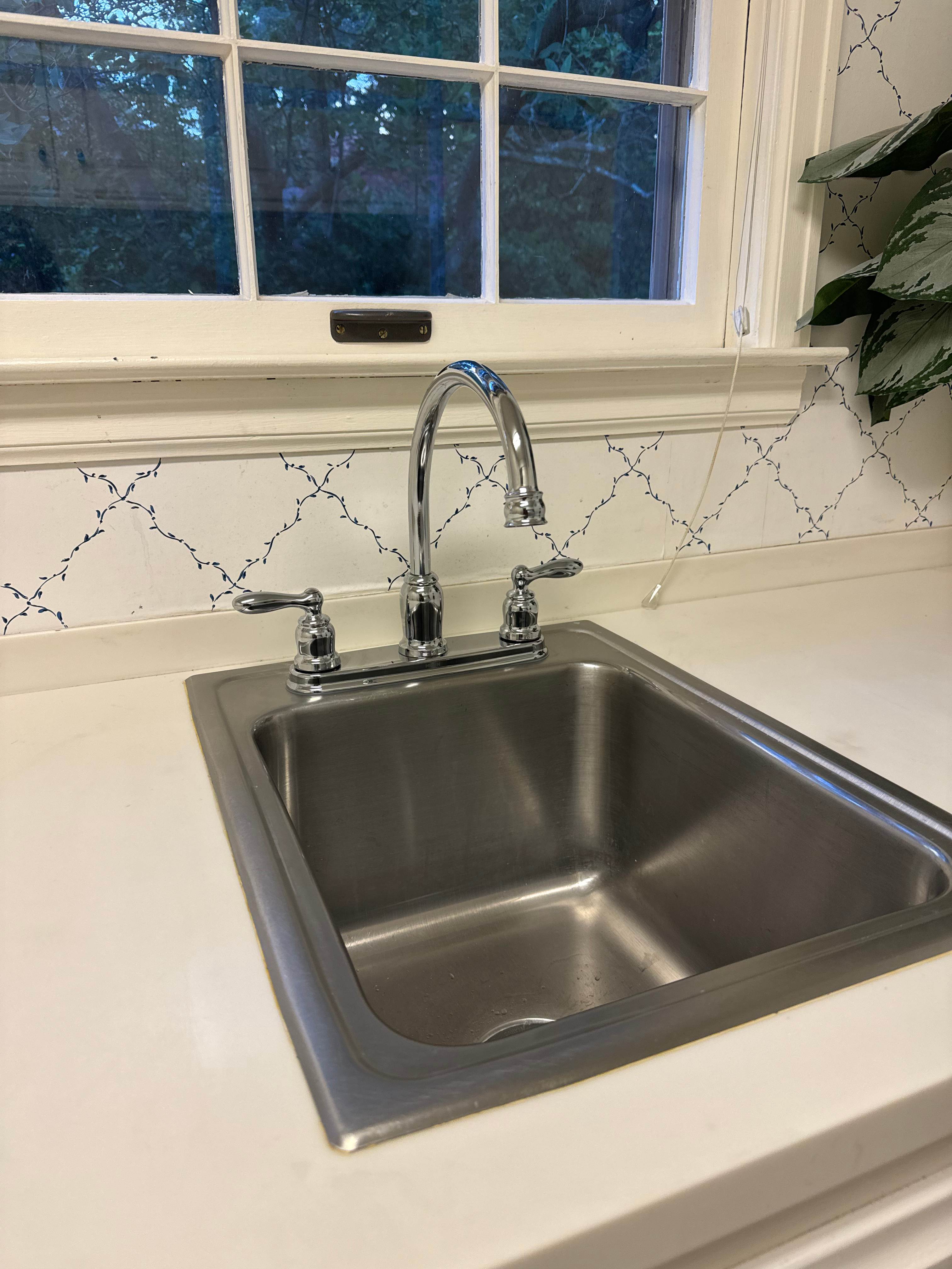 Stainless undermount kitchen sink with chrome gooseneck faucet on white quartz counter.