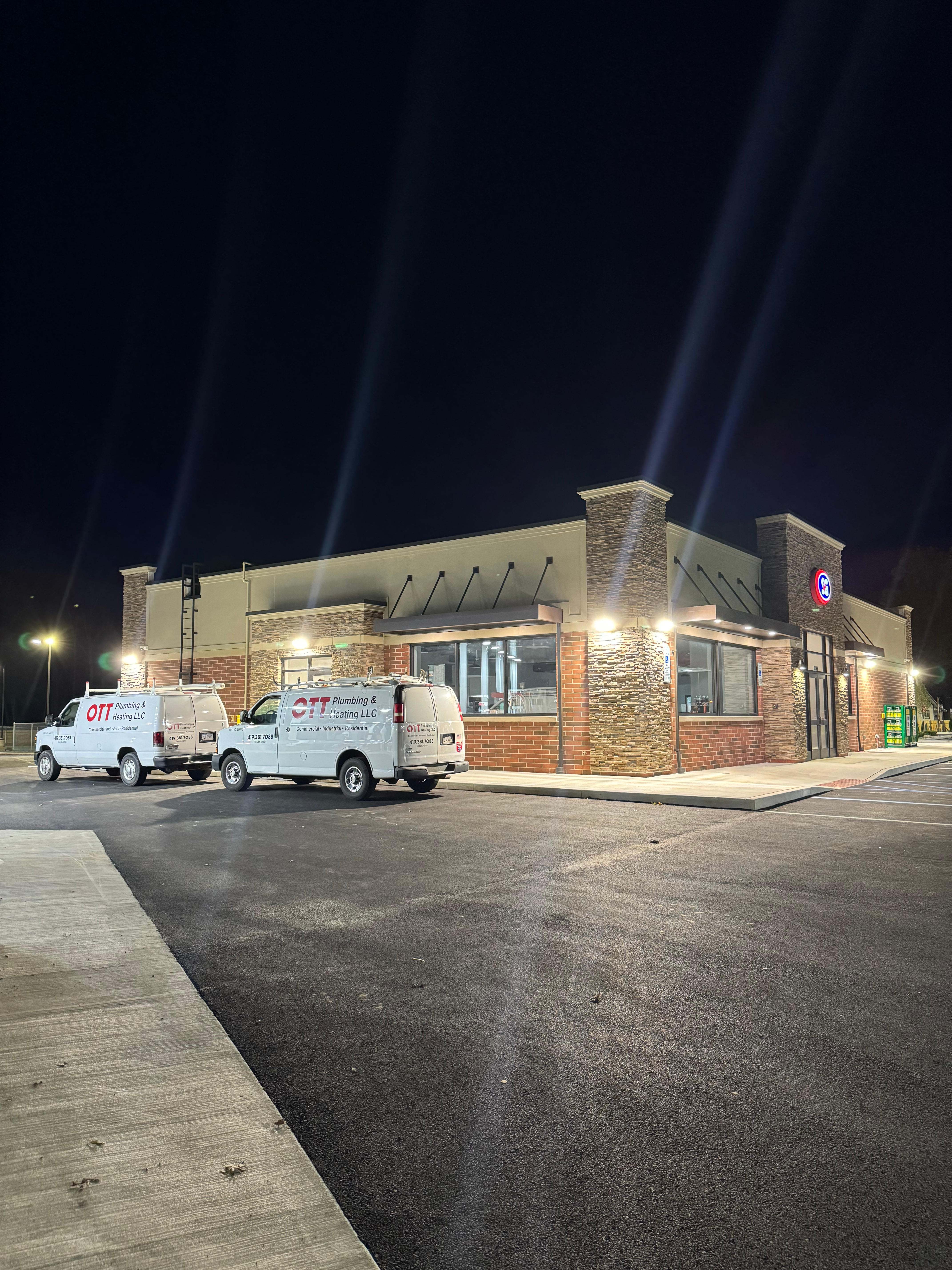 Two branded Ott Plumbing and Heating service vans parked outside a Toledo commercial building at night.
